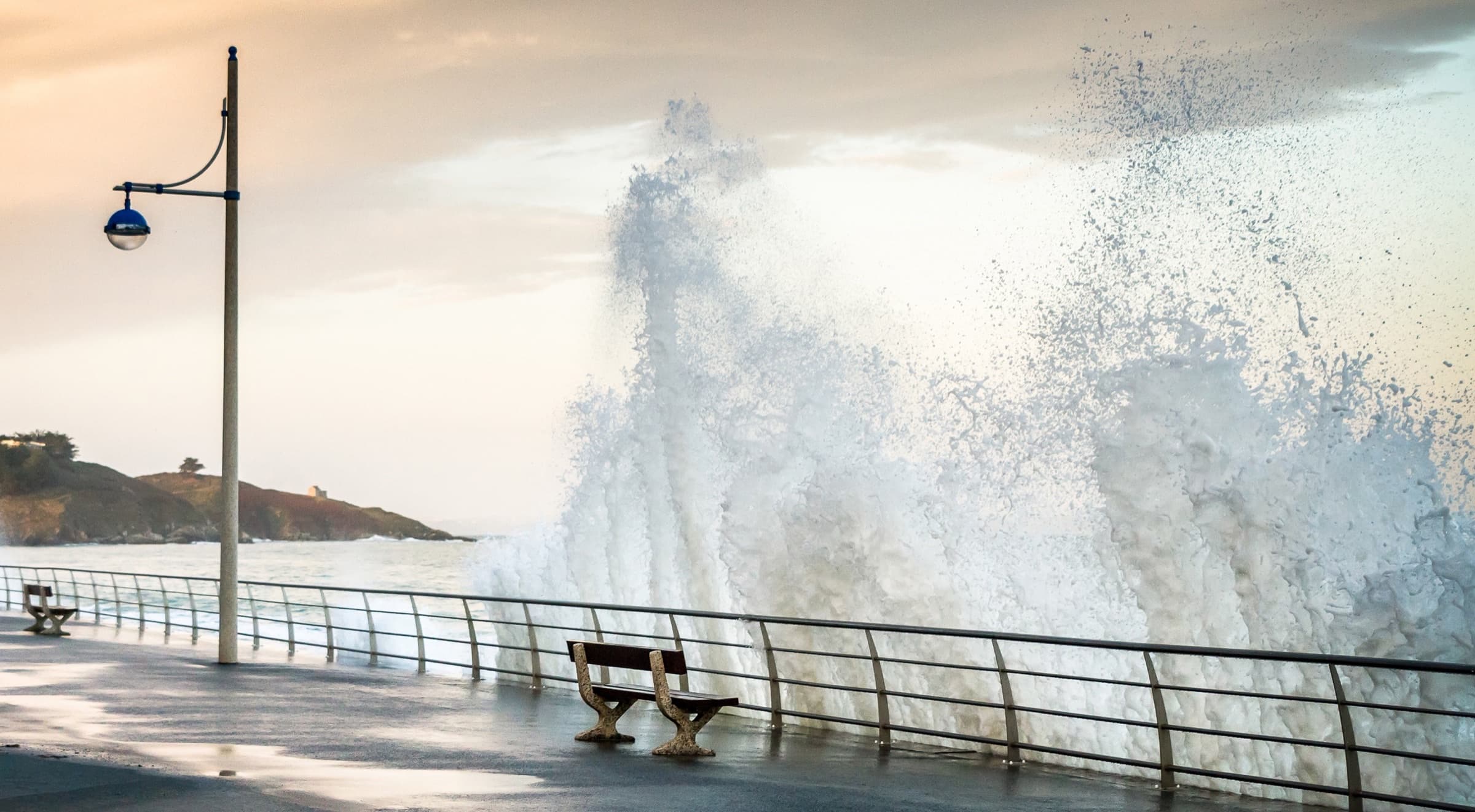 Dramatic wave crashing against seawall promenade